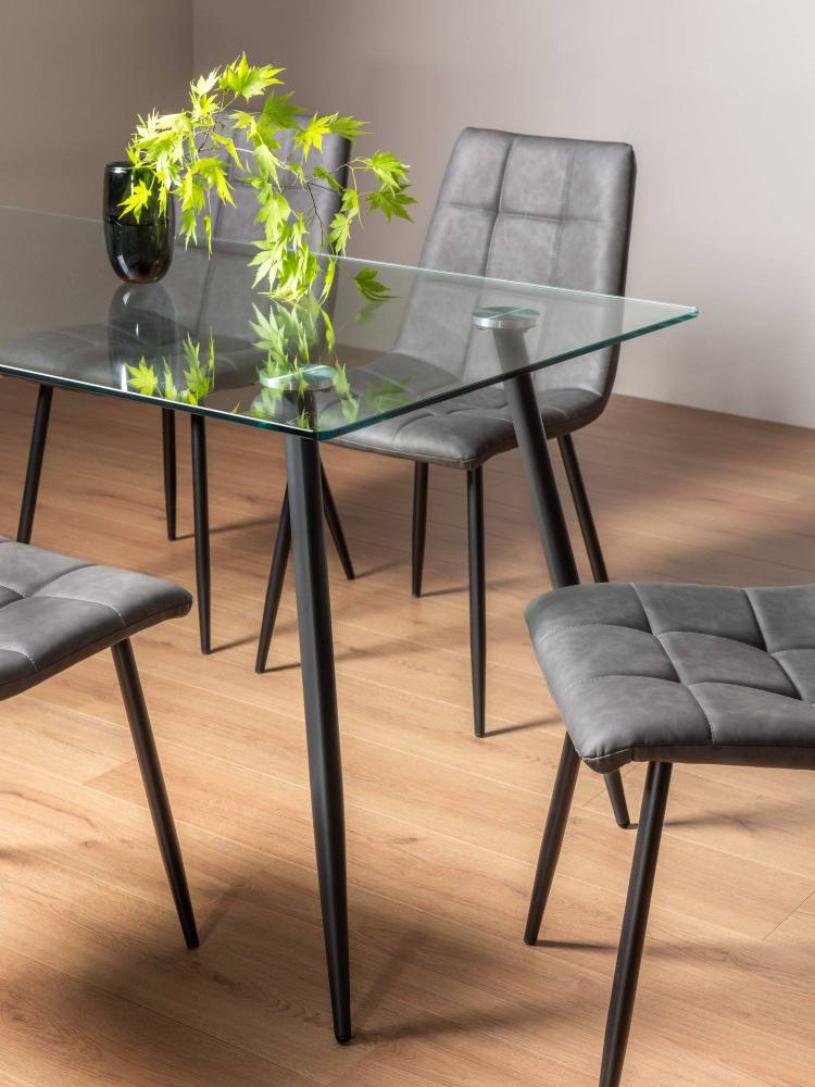 Close Up of the Bentley Designs Martini Clear Tempered Glass 6 Seater Dining Table & 4 Mondrian Dark Grey Faux Leather Chairs with Sand Black Powder Coated Legs